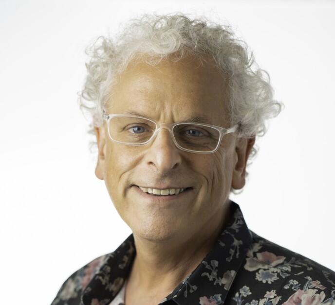 Andy Sack — curly grey hair, clear-frame glasses, floral shirt, smiling against a white background